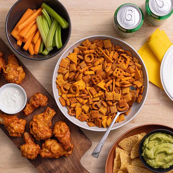 Chex Mix in a bowl surrounded by chicken wings and veggies